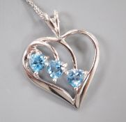 A modern 9ct white gold and three stone blue topaz set stylised heart shaped, pendant, 25mm, on a