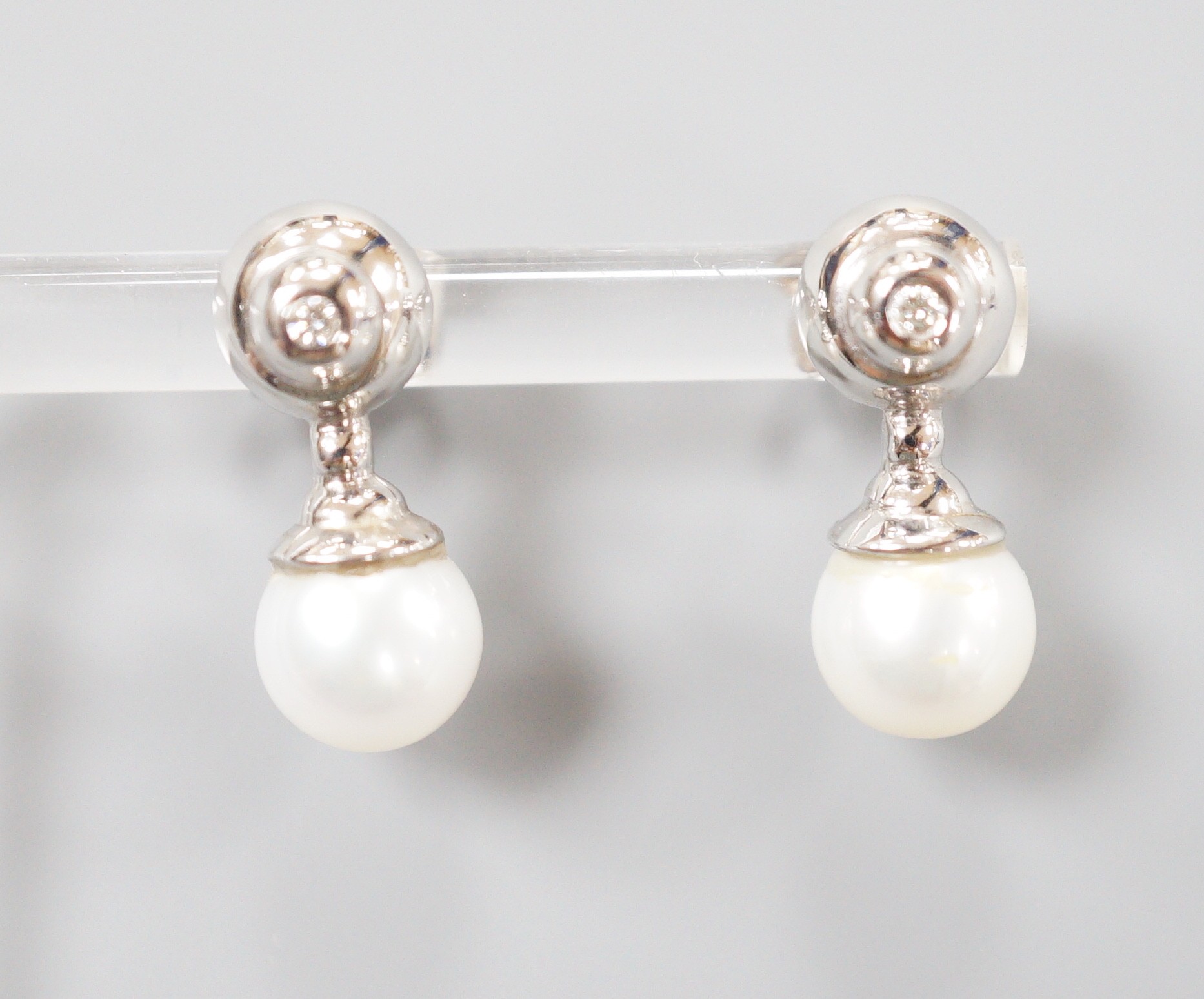 A modern pair of 198ct white gold cultured pearl and single stone collet set diamond ear studs,