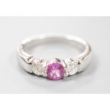 A modern platinum, single stone pink sapphire and two stone diamond set ring, size M/N, gross weight