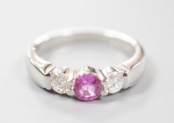 A modern platinum, single stone pink sapphire and two stone diamond set ring, size M/N, gross weight