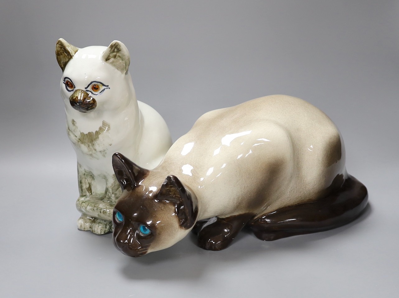 A Kensington ceramic lurking Siamese cat with blue glass eyes by Winstanley, together with