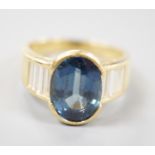 A modern 18ct gold and single stone oval cut sapphire set ring, with baguette cut diamond set