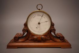 A Negretti & Zambra brass cased barometer on carved mahogany stand, 31cm wide