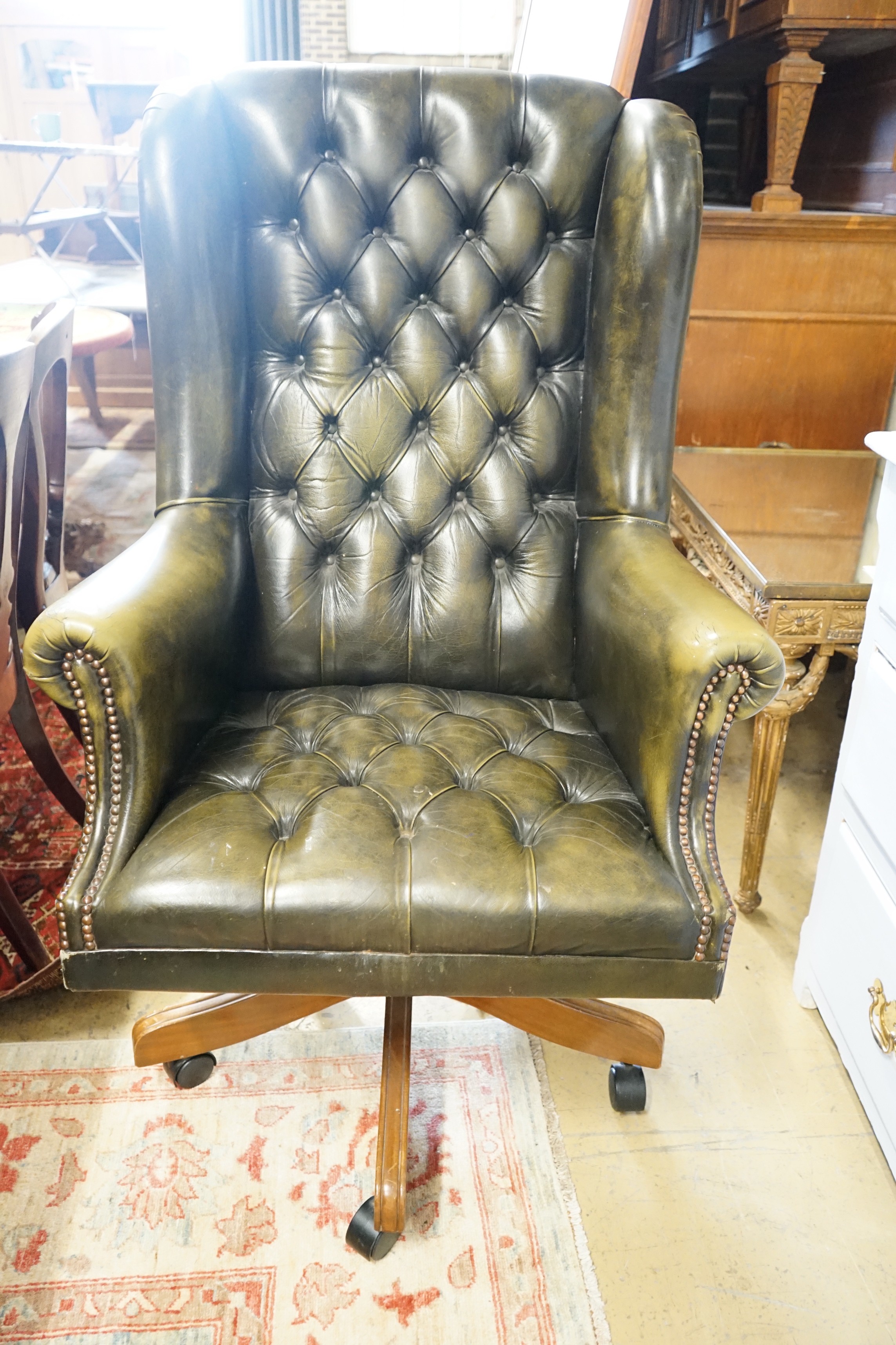 A Victorian style buttoned green leather swivel desk wing armchair, width 78cm, height 120cm