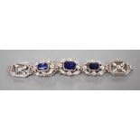 A modern 9ct white metal and three stone emerald cut synthetic sapphire set pierced link bracelet,