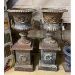 A pair of Victorian style cast iron campana garden urns on square plinths, height 110cm