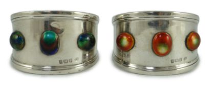 Two similar Edwardian Arts & Crafts silver and enamelled napkin rings, each set with three