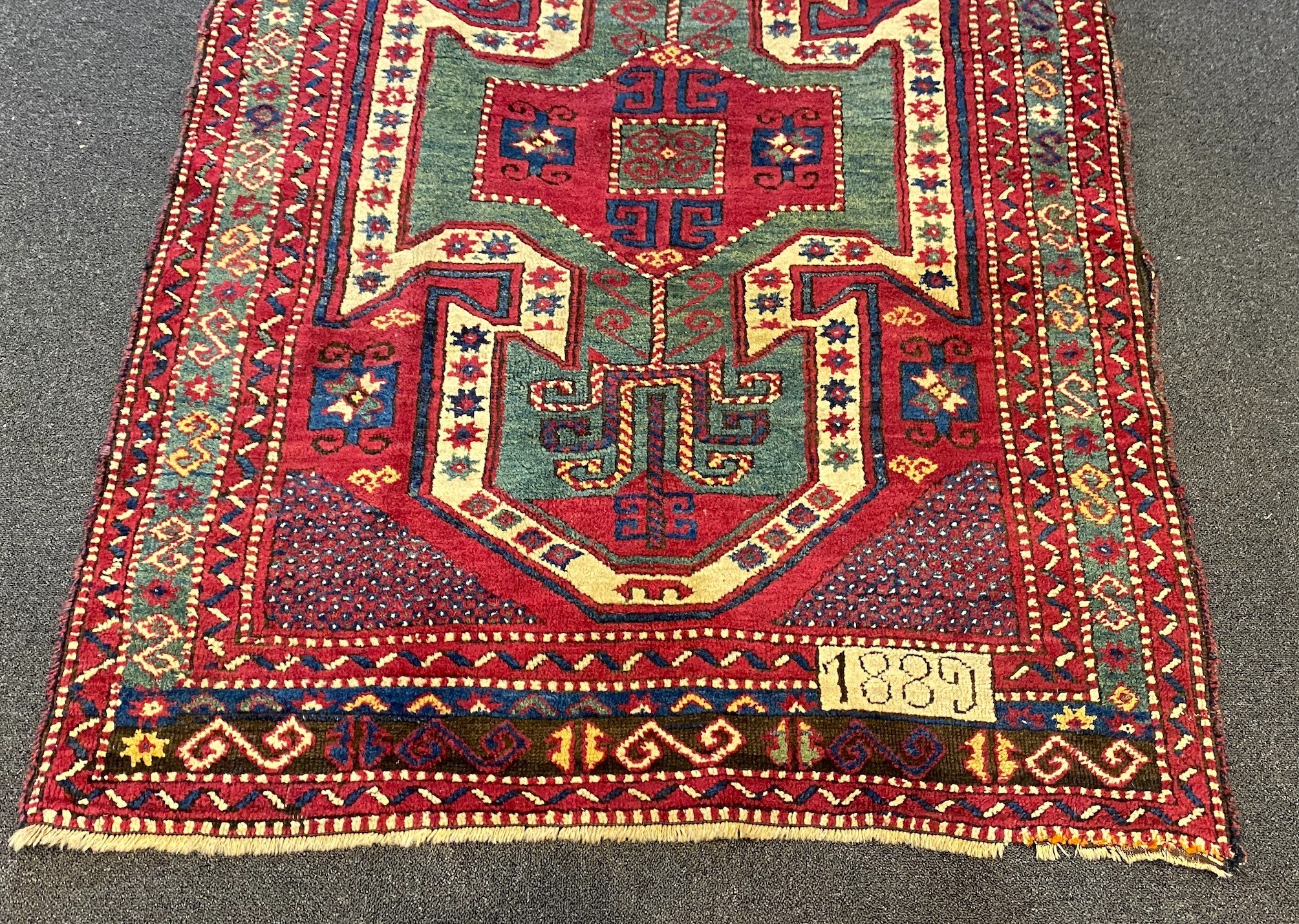 An antique Kazak red ground rug, with double shield motif within a hooked geometric field and triple - Image 2 of 5