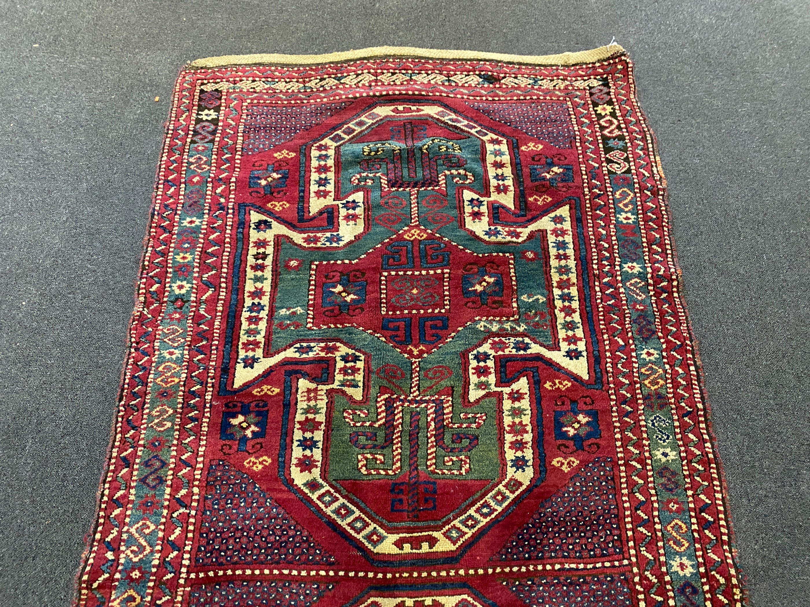 An antique Kazak red ground rug, with double shield motif within a hooked geometric field and triple - Image 4 of 5