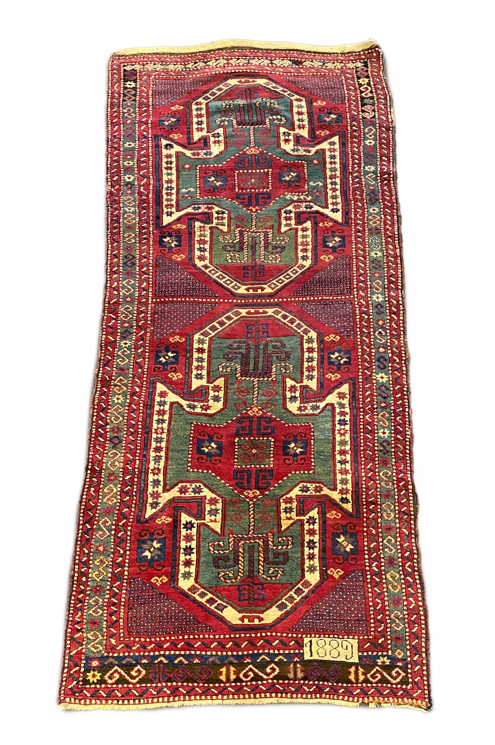 An antique Kazak red ground rug, with double shield motif within a hooked geometric field and triple