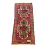 An antique Kazak red ground rug, with double shield motif within a hooked geometric field and triple