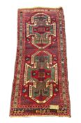 An antique Kazak red ground rug, with double shield motif within a hooked geometric field and triple