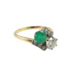 A gold, emerald and diamond set two stone cross-over ring, with diamond set shoulders, the diamond