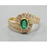 A modern 18ct gold, collet set oval cut emerald and diamond cluster set crossover ring, size N,