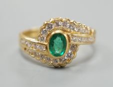 A modern 18ct gold, collet set oval cut emerald and diamond cluster set crossover ring, size N,