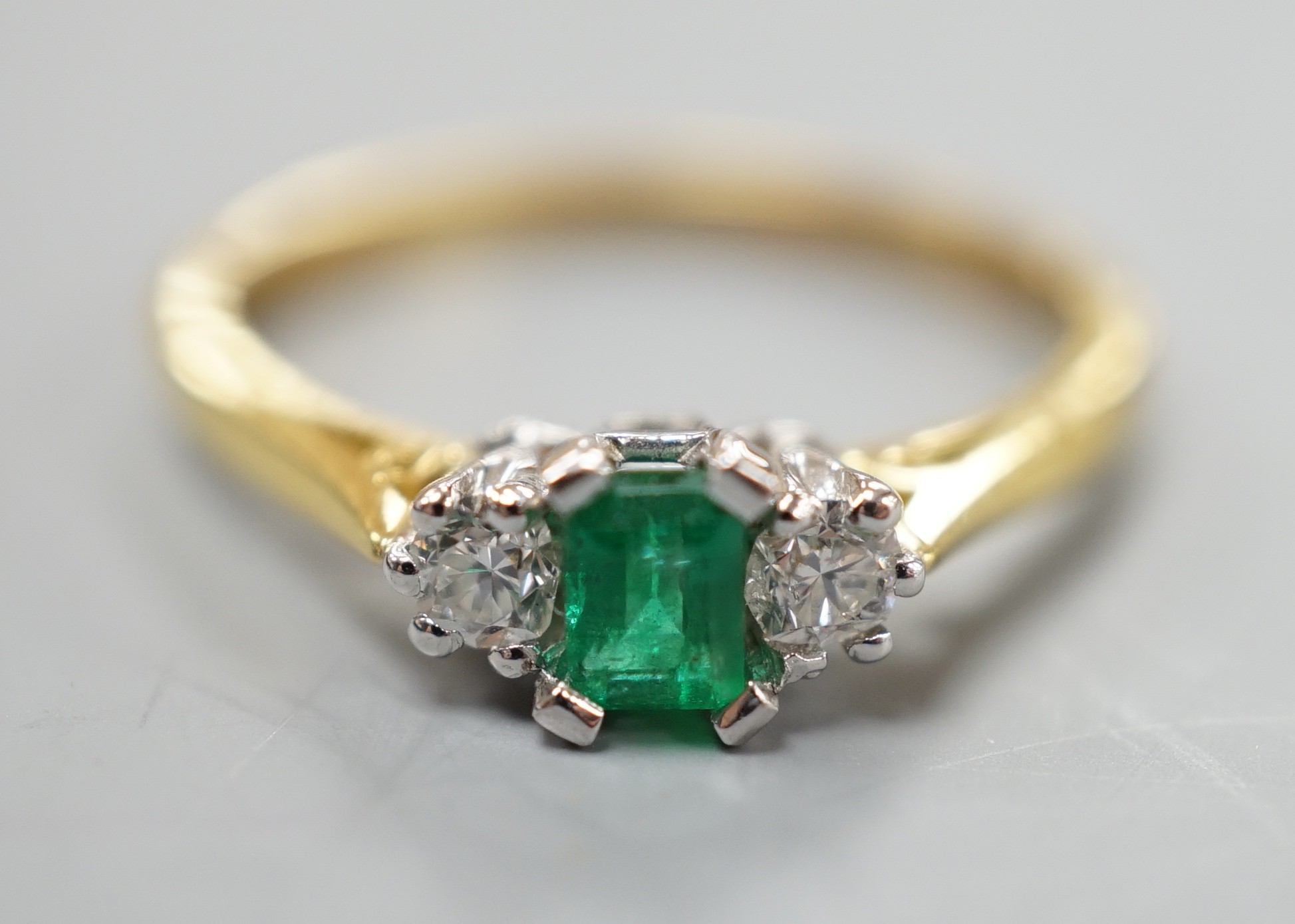 A modern 18ct gold, emerald and diamond set three stone ring, size N, gross weight 2.6 grams.