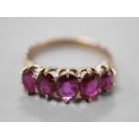 An early 20th century yellow metal and graduated five stone ruby set half hoop ring, size O, gross