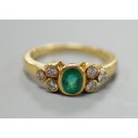 A modern yellow metal and collet set oval cut emerald ring, with six stone diamond set shoulders,