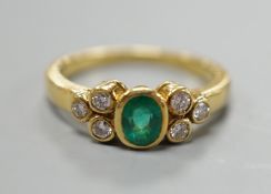 A modern yellow metal and collet set oval cut emerald ring, with six stone diamond set shoulders,