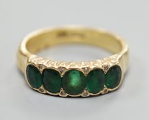 A modern 18ct gold and graduated five stone emerald set half hoop ring, with diamond chip spacers,