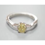 A modern platinum and single stone fancy yellow diamond set ring, with trapeze cut diamond set