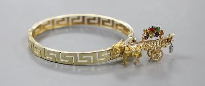 A modern yellow metal hinged bangle with Greek Key decoration and a 9ct donkey and cart charm, gross