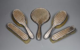 A George V silver and yellow metal five piece dressing table mirror and brush set, by Charles &