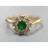A modern 18ct gold, emerald and diamond set circular cluster ring, size M, gross weight 3 grams.