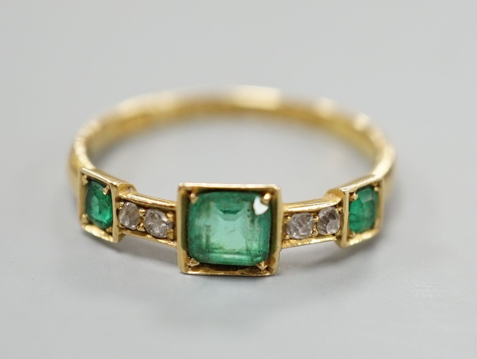 A George V 18ct gold, three stone emerald and four stone diamond chip set half hoop ring, size L,