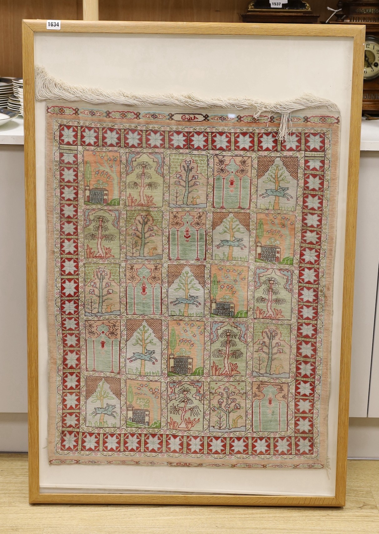 An Eastern framed silk rug depicting trees amimals and buildings, 86 cms high x 67cms wide