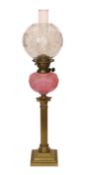 An Edwardian brass Corinthian column oil lamp with opaque pink glass reservoir, etched glass globe