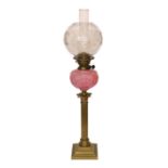 An Edwardian brass Corinthian column oil lamp with opaque pink glass reservoir, etched glass globe