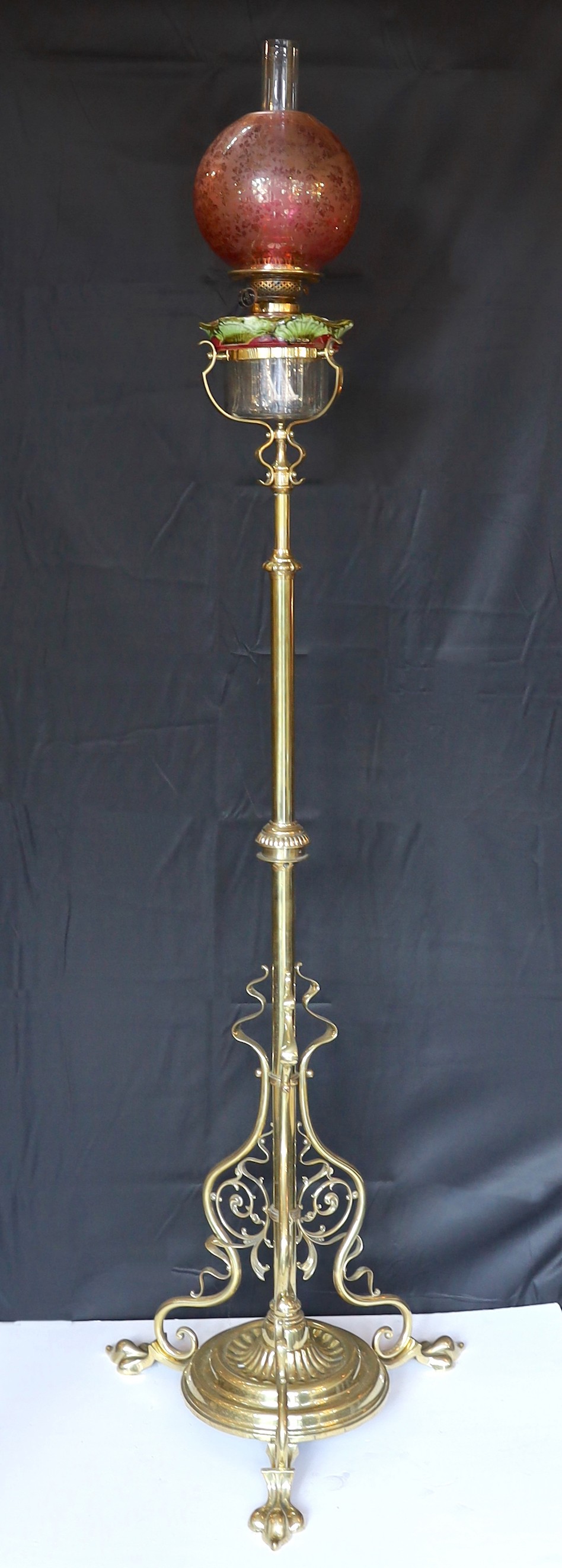 An Edwardian brass telescopic oil lamp standard, with later edged cranberry glass shade and duplex