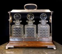 An Edwardian silver plated mounted oak tantalus fitted with three cut glass decanters, width