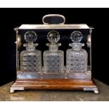 An Edwardian silver plated mounted oak tantalus fitted with three cut glass decanters, width