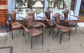 A set of six French wrought iron and brown leather elbow chairs, with brass ball finials, four