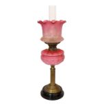 A late Victorian brass oil lamp with opaque pink glass reservoir, duplex mechanism, cranberry tinted