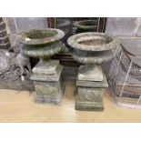 A pair of circular reconstituted stone campana garden urns on square plinths, one urn a.f., diameter