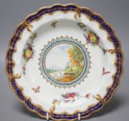 A Worcester plate painted with a landscape surrounded by fruit and moths under a blue and gilt