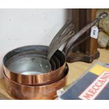 A matching set of five graduating copper pans and an oak pan rack