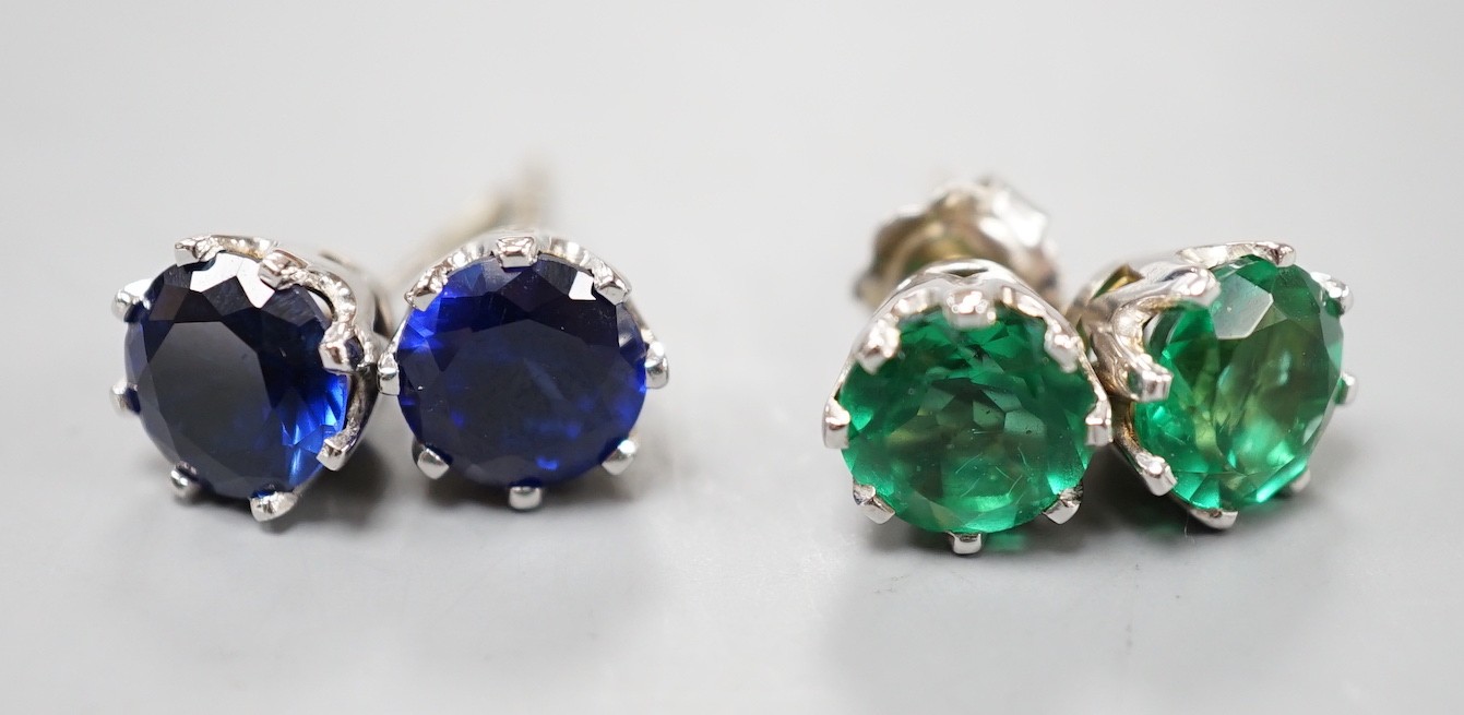 Two pairs of white metal ear studs, one set with green paste, the other with synthetic sapphires,