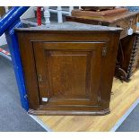 A small George III oak wall hanging corner cupboard, with hinged panelled door and shelved interior,