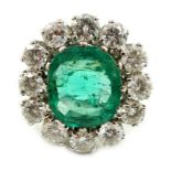 An impressive platinum, emerald and diamond set oval cluster dress ring, the emerald measuring