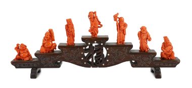 A Chinese or Japanese set of seven coral figures of immortals, on a stepped wood stand, 43cm wide,