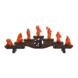 A Chinese or Japanese set of seven coral figures of immortals, on a stepped wood stand, 43cm wide,