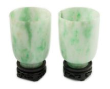 A pair of Chinese jadeite cups, the white stone with emerald green veining, 6.2cm high, wood stands,
