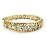 A pierced gold and twelve stone oval white opal set hinged bangle, interior diameter 57mm, gross