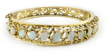 A pierced gold and twelve stone oval white opal set hinged bangle, interior diameter 57mm, gross