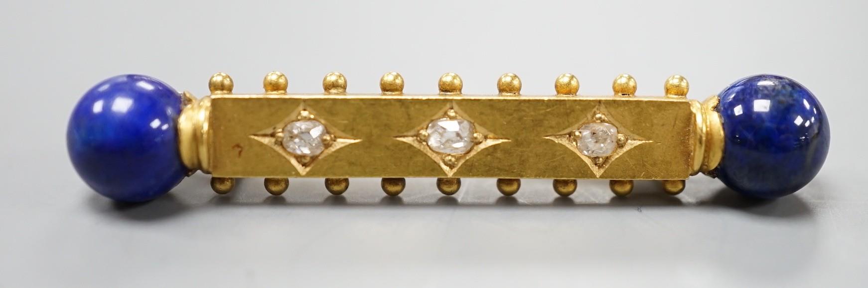 A yellow metal and three stone diamond set bar brooch. with lapis lazuli bead set terminals, 43mm,