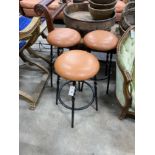A set of three wrought iron and tan leather stools, height 64cm